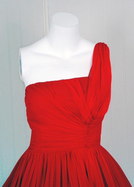 Breathtaking 1950's party dress fashioned from fully-lined flowing silk-chiffon. This garment is so fresh and modern with its vibrant ruby-red color and asymmetric design! This beauty combines a fetching, girlish appeal with a woman's allure— a