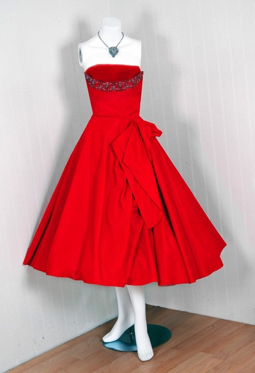 Breathtaking 1950's party dress fashioned from rich silk-taffeta. This garment is so fresh and modern with its vibrant ruby-red color and asymmetric draped-design! This beauty combines a fetching, girlish appeal with a woman's allure— a dynamite