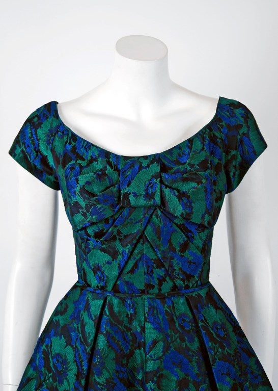 Les premiers vêtements de Michael Novarese sont incroyablement rares et sont rarement mis en vente. Dans cette magnifique robe de soirée en soie croisée à imprimé floral bleu-vert de la fin des années 1950, la construction détaillée et l'attention