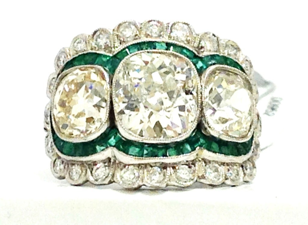Spectacular ring, composed of three antique cushion European cut diamonds, accented by an elegant emerald channel set bezel, each emerald is calibrated to fit channel, and an additional diamond halo, where is each single cut diamond is individually