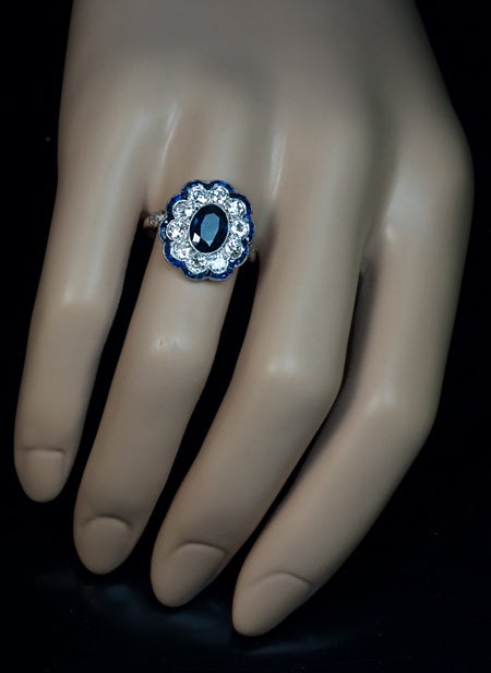 This finely crafted fancy cluster ring features an oval sapphire center in a millegrain platinum setting, framed by bright white and sparkling ten Old European cut round diamonds which, in turn, are outlined with a curvaceous border of tiny
