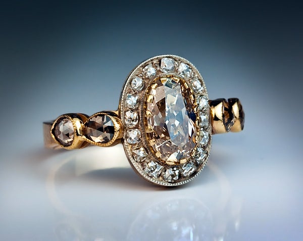 The ring is centered with an antique cushion cut 1.34 carat natural fancy orange brown diamond in a yellow gold prong setting, framed by sixteen (16) French cut white diamonds set in silver over rose gold.

The shoulders of the ring are