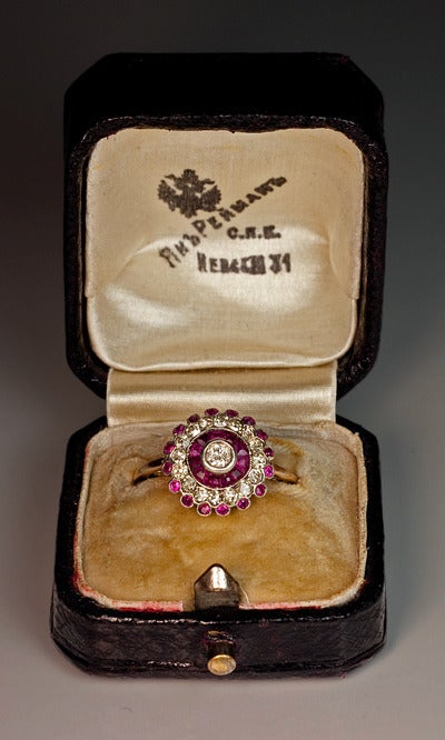 Handcrafted  in St. Petersburg between 1908 and 1917.

The central diamond is surrounded by eleven channel set calibre cut rubies encircled by a row of sixteen single cut diamonds. 

The edge is highlighted with sixteen round rubies. All stones