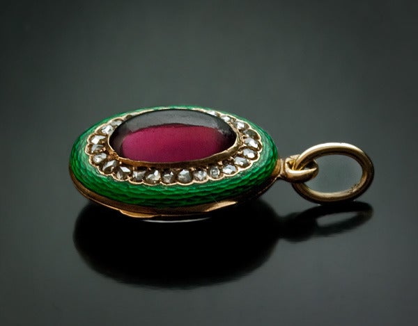 circa 1850

An oval shaped pendant set with a cabochon cut almandine garnet (carbuncle),  surrounded by a row of 26 rose cut diamonds, within a vivid green guilloche enamel frame.

The back cover of the pendant is fitted with two glazed