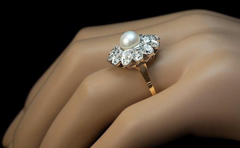 This large and elegant dress ring is centered with a 7 mm natural pearl encircled by two rows of old single cut diamonds.

The 24 diamonds are of G-H color and mostly VS clarity.  

The estimated combined weight is 1.56 ct.

The ring is hand