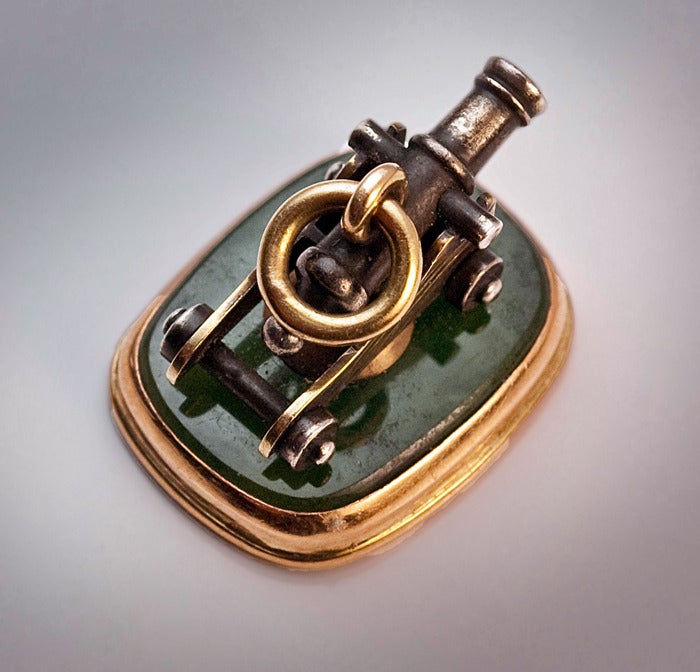 An Antique Watch Fob by Peter Carl Faberge

 St. Petersburg, circa 1885

 The fob pendant is designed as a miniature navy cannon.  The realistically modeled parcel gilt silver cannon is mounted on a piece of carved nephrite set in 14K rose gold.