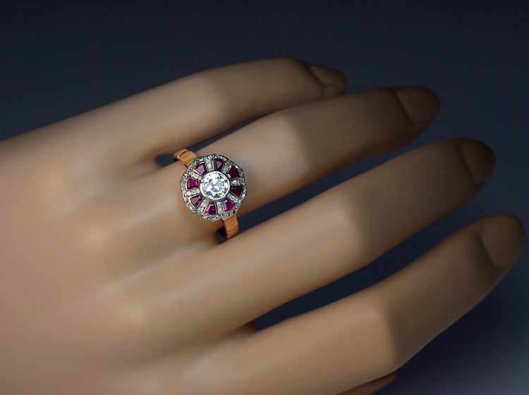 circa 1910

The ring is designed as a stylized flower centered with a bezel set Old European cut diamond (approximately 0.63 ct, J color, VS2 clarity) with six tapered calibre cut natural ruby 
