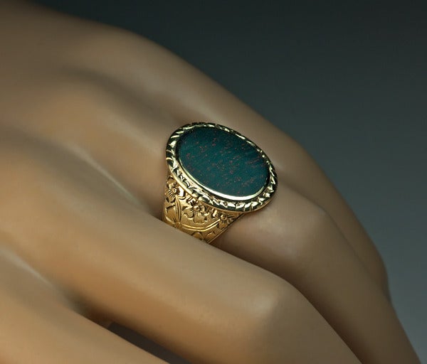 A Victorian era antique 14K greenish yellow gold ring is set with a flat oval heliotrope - a variety of chalcedony, also known as bloodstone. This stone is a classical example of a bloodstone - very dark green with numerous fine inclusions of red