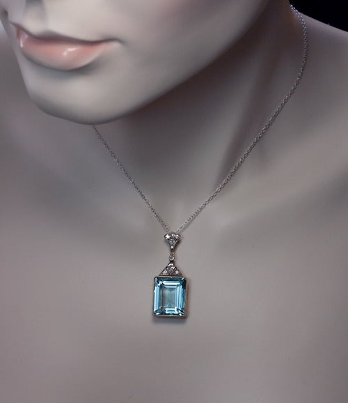 Moscow, circa 1930

A richly saturated cool blue emerald cut aquamarine (18 x 14 x 8.8 mm - approximately 15.19 ct) in a yellow 14K gold milgrain setting crowned by a triangular art deco style diamond-set mount and a plume shaped diamond bail. The