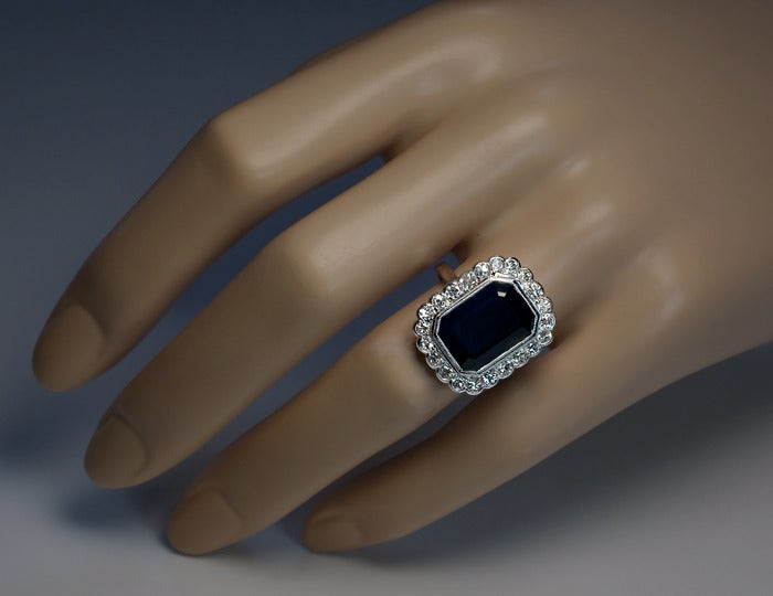 The ring features an emerald-cut midnight blue 7.59 ct natural sapphire surrounded by 22 Swiss cut sparkling white diamonds (estimated total weight 1 carat). 

The shank is struck with a dog's head French platinum mark.

Height - 20 mm (13/16