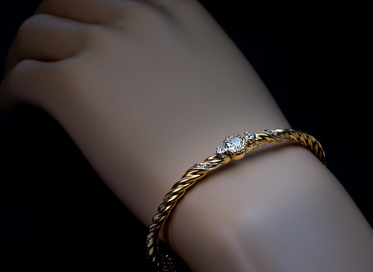 An Elegant Antique Swirl Bangle Bracelet

Austro-Hungarian Empire, Prague, circa 1890

The twisted 14K gold bracelet is centered with a large yellowish old mine diamond (0.92 ct, M color, SI1 clarity) 
flanked by two smaller white diamonds and