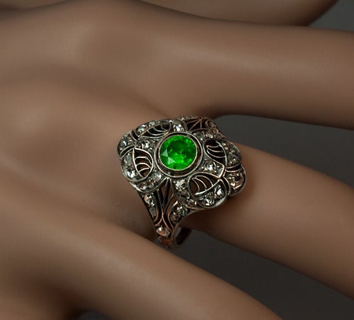 Moscow, circa 1930

 An elaborate openwork silver and gold ring features a very fine vivid green Russian demantoid garnet in a surrounding of 34 rose cut diamonds.

 The demantoid is 5.6 x 3.4 mm, approximately 0.75 ct.

 Estimated total
