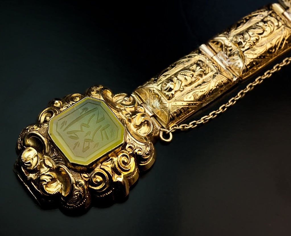 An ornate hollow 18K gold bracelet with embossed and hand engraved decorations is set with an octagon cut jade engraved with an unidentified Eastern script.

Weight 14.86 grams

Length 16,5 cm  (6 3/4 in.)