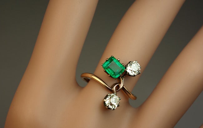 circa 1900

 A 14K  gold ring is designed as a stylized gem-set flower in Art Nouveau taste.

 The ring is set with a beautiful Colombian emerald  (6.3 x 5.1 x 3.4 mm, approximately 0.76 ct) and two antique cushion cut diamonds set in silver