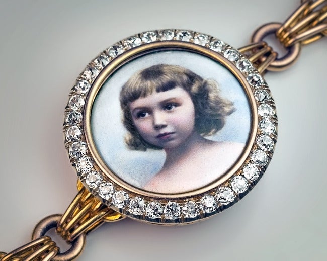 A Russian Imperial era 14K gold link bracelet features a painted enamel portrait miniature (diameter 19 mm - 3/4 in.) of a young girl in a diamond-set bezel. The superbly painted portrait miniature is surrounded by 34 old mine and old single cut