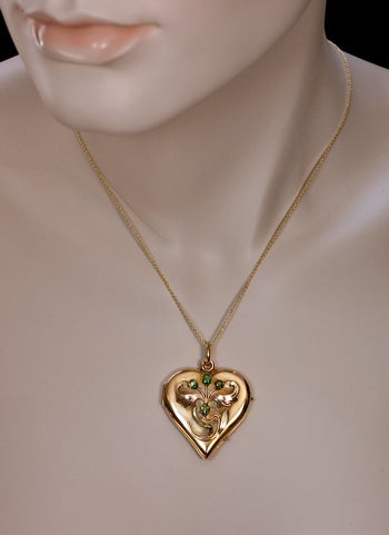 An Antique Russian Art Nouveau Locket Pendant.

A polished yellow gold heart shaped locket is decorated with a chased rose and green gold Art Nouveau flower embellished with four Russian Uralian demantoid garnets.

The interior is set with two