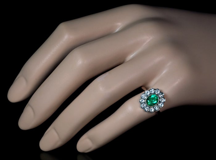 A vintage emerald and diamond cluster ring centered with an old mine oval emerald (approximately 1.25 ct) of a nice color, 

surrounded by a row of twelve old cut diamonds which are set in silver over rose gold. 

The combined weight of the