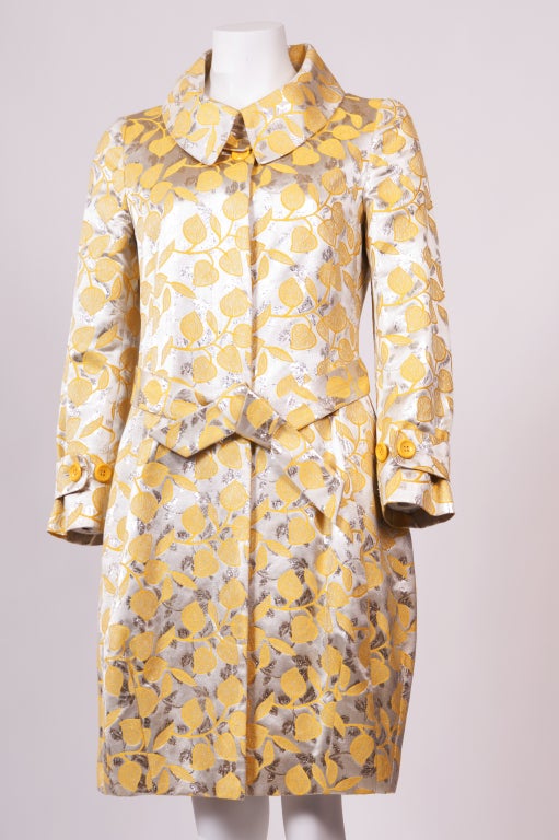 A classic Moschino gold and yellow floral printed jacquard coat features a concealed button fastenings through front with a waist belt.  Button fastening tabs at cuff.  Fully lined.