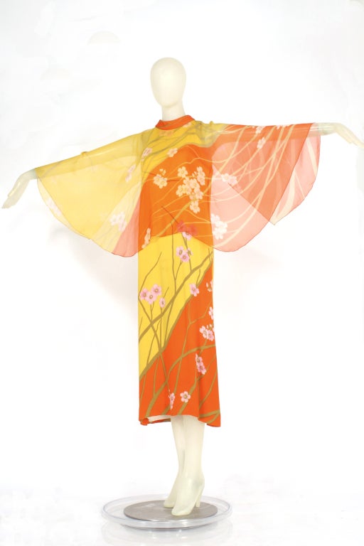Hanae Mori
1970's Hanae Mori bold print silk chiffon dress. Orange and yellow floral pattern. Sheer cape. Ankle Length. Ties in back at collar. Zips up the back. Very good vintage condition.

Store Location:

DEVORADO
436 E.9th St.
NYC, NY