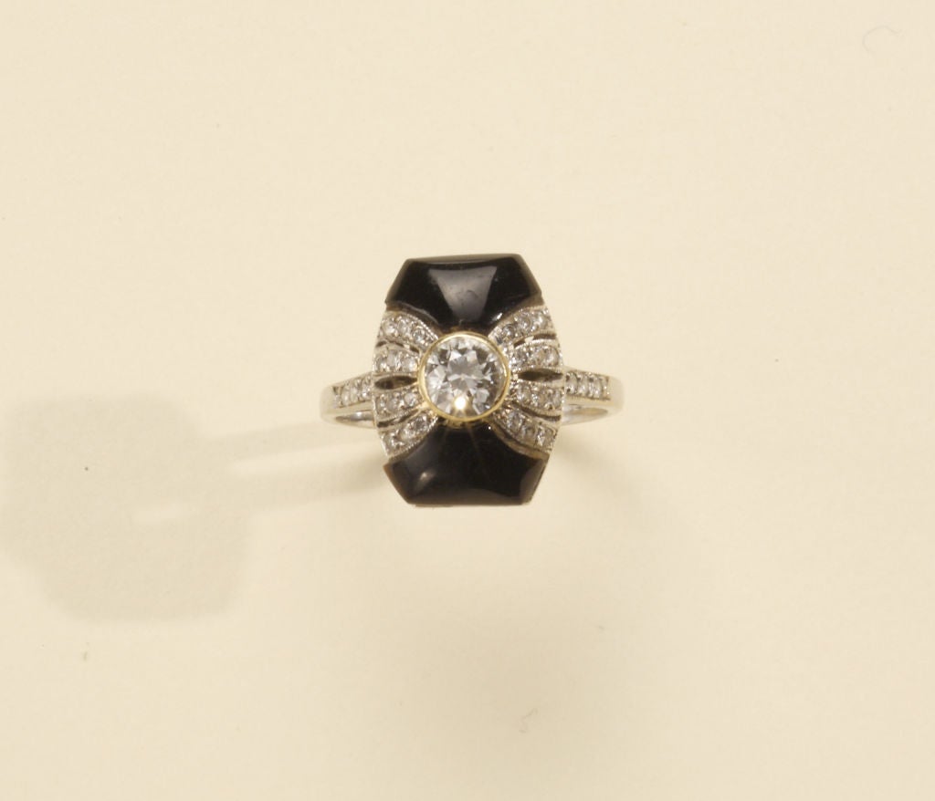 A cushion shaped onyx is tied in a bow of european full cut diamonds that spill to the shoulders of this elegant Art Deco ring. Set mid center in a gold bezel, is a round european cut diamond of approximately .50 cts in weight. The ring setting is