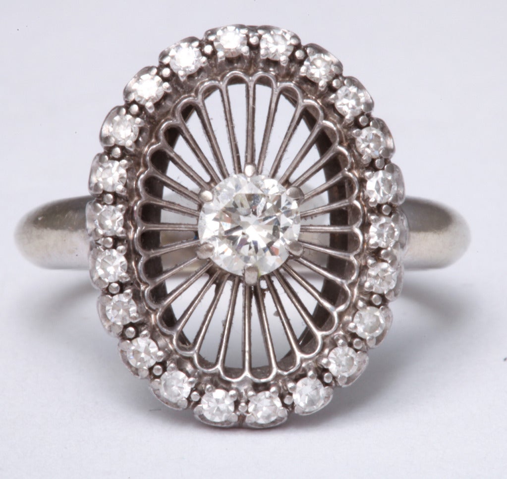 Sparkling and white, this delicate ring of diamonds attracts attention with a statement of grace and singular design. Rays radiate from the encircling diamonds to the center diamond of approximately .70 cts. A generous rounded shank of 14kt white