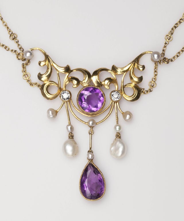 : This romantic gemstone, gold necklace is textbook art nouveau made in the USA. Curling leaves swirl and loop toward a central heart shaped vine that supports lush amethysts, diamonds and pearls. Swags of gold chain that have been detailed for