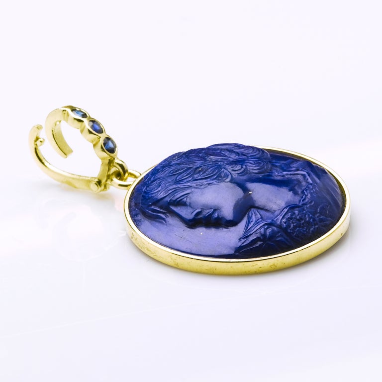 Exquisitely detailed lapis lazuli carving in high relief of a young lady in the style of Fragonard with a mythological city as her crown. Pendant is set in an 18 Karat gold frame with .30 cts blue sapphire which opens to hang from your necklace.