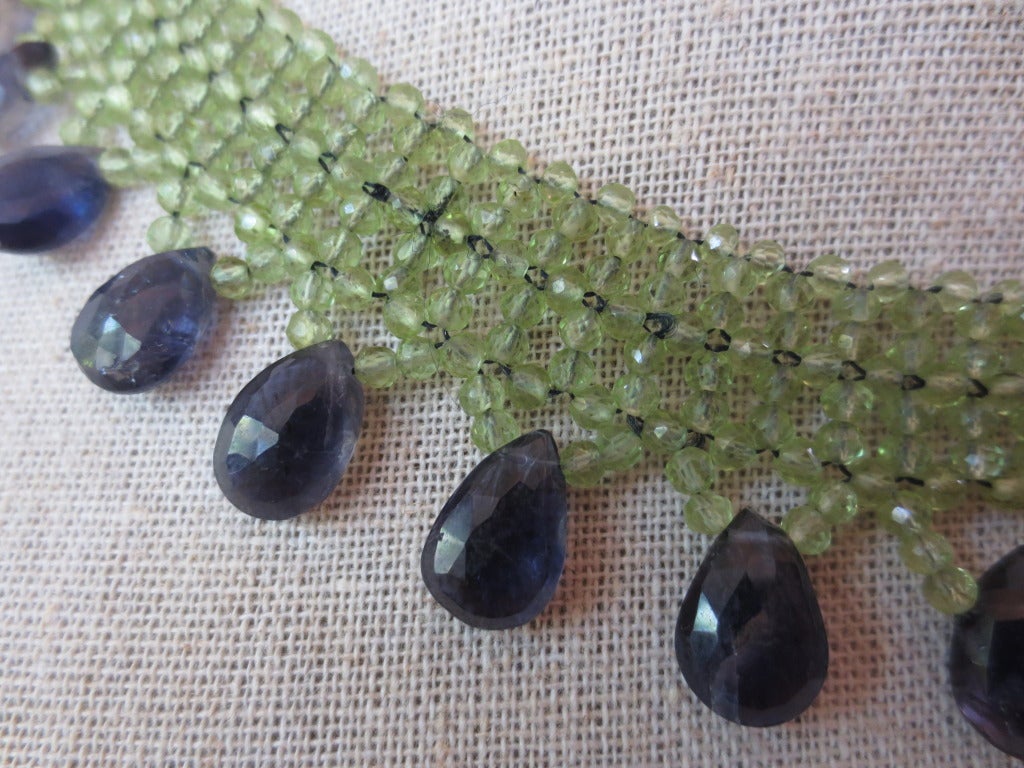 This hand woven necklace is made using 2-3 mm peridot faceted beads to create a lace-like design that perfectly fits the collar. Necklace is tapered in design to fit along the curve of the neckline. Graduated iolite teardrop briolettes hang from the