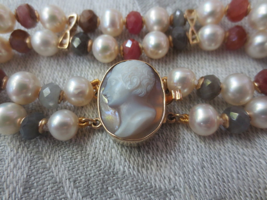 This unique bracelet is made with an antique shell cameo. Set in a 14k gold clasp, the cameo carving is of a male profile. The iridescent shell background is complimented by the rough ruby, rough sapphire and pearl bracelet. The bracelet is made of