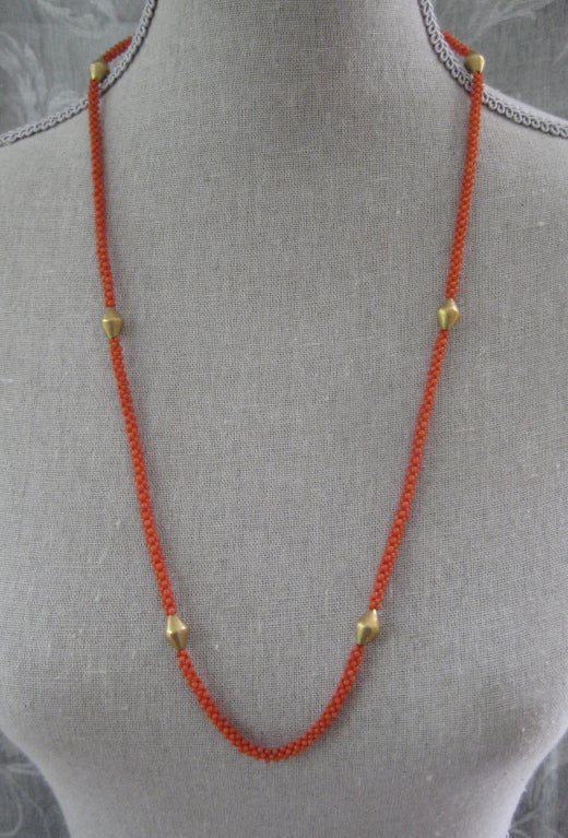 Hand woven coral necklace is detailed with antique Old English 18k gold plated beads. Unique hand made clasp allows abilty to wrap around neck. Necklace measure 30 inches in length. Tassel is removable by 14k gold finding and measures 3 3/4 inch.