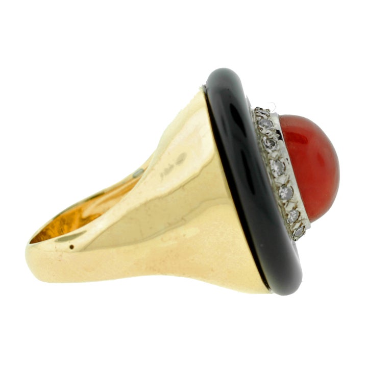 An unusual and stunning Vintage coral and onyx ring from the 1960s! Crafted in 14kt yellow gold, the design features a round ring of carved onyx which surrounds a single cabochon coral link at the center. The coral displays a vibrant, rich color and