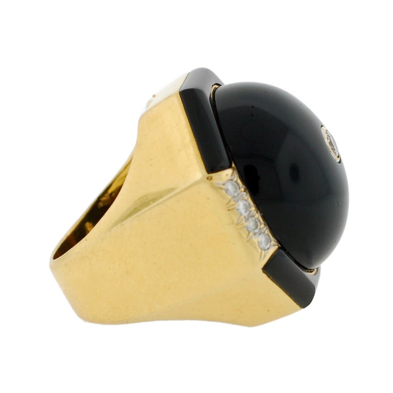 A fabulous Vintage cocktail ring from the 1960's! This bold piece is made of 18kt yellow gold and is particularly large in size. At the center of the ring is a large, round cabochon onyx stone, which has a bezel set diamond inlaid in its center. The