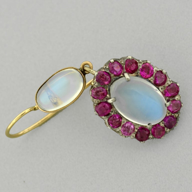 A beautiful pair of moonstone and ruby earrings from the Art Nouveau (ca1910) era! These charming earrings are made of sterling topped 14kt gold and hang from 14kt yellow gold gold earring wires. Each earring begins with a topper, which features a