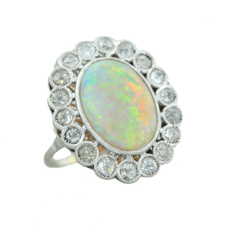An breathtaking opal and diamond ring from the Edwardian era (ca1910)! This gorgeous piece is made of platinum and has a large oval shaped opal cabochon set in the center. The opal is mesmerizing and has vibrant hues of greens, yellows, blues,