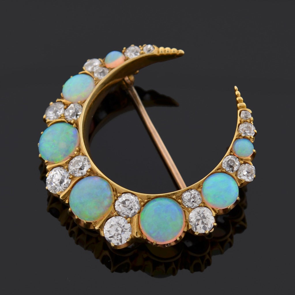 A breathtaking opal and diamond crescent pin from the Art Nouveau (ca1900) era! Made of 14kt yellow gold, this exquisite crescent moon piece adorns 7 vibrant opals which alternate with rows of 16 old Mine Cut diamonds. The opals and diamonds