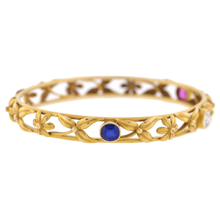 A gorgeous multi-stone bangle bracelet from the Art Nouveau (c1900) era! Made of vibrant 14kt yellow gold, this fabulous piece is decorated with a lovely floral motif which carries around the entire surface. The beautiful flowers and leaves rest