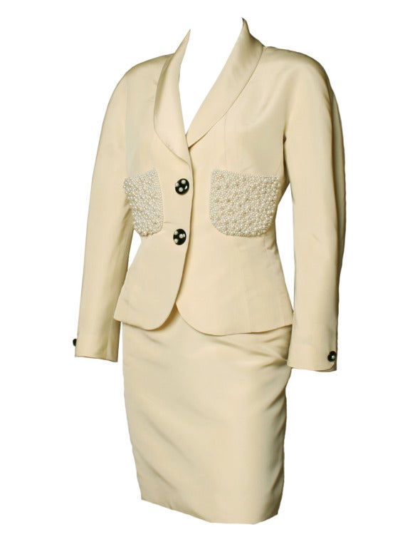 Synonymous of elegance and glamour, Coco Chanel masters another great piece with this cream silk with pearls detail skirt and blazer set. Jaw-dropping blazer features exquisite detail pearl work on each pocket providing a soft fashion to this Chanel