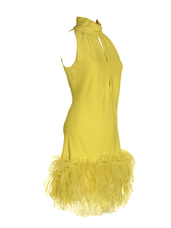 Turn heads with this show stopping 1960's yellow crepe dress with an ostrich feather hem.  This impressive shift dress is sleeveless with a double keyhole neckline.  The stand collar has a fine yellow stitching detail.  The allure continues with the