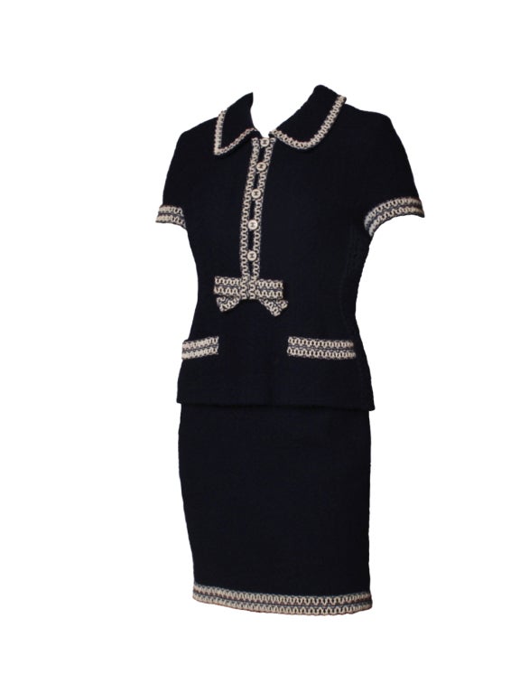 Master effortless elegance with this 1980's Chanel dark navy and white set. Crafted from dark navy boucle and adorned with a rubber criss cross trim, this suit set features a collared double-breasted jacket with front pockets and white bow with a