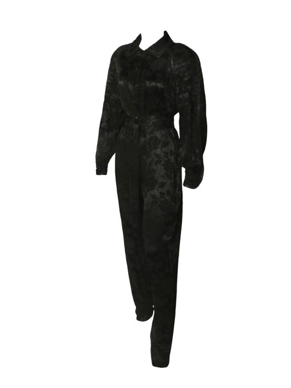 This 1980s Koos Couture black silk with leather trim jumpsuit is the perfect blend of style and comfort.  Trimmed with a intricate leather detail, This Koos Couture jumpsuit features a black jacquard silk, rhinestone buttons down the center front,