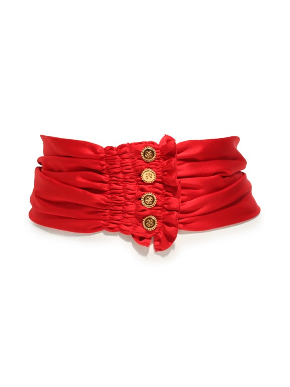 Add sophistication and elegance to your accessories collection by investing in this Chanel red satin sash. This scarlet red sash features 4 leaf clovers engraved into gold buttons and shirring details at each end providing a gather illusion