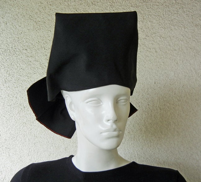 Adrian Original high fashion toque hat fashioned of black faille in a four(4) corner high top pulled and folded into a back bow. Bow enhanced by subtle red trim.  This style was often used in pairing with an Adrian suit adding just the right touch