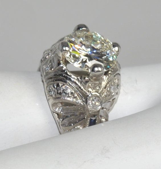 This platinum mounting has beautiful filigree work depicting bows that really captivate the art deco period. It has a 1.69 carat Old European cut diamond that has approximate GIA color and clarity of I/VS1. It is set with four prongs and slightly