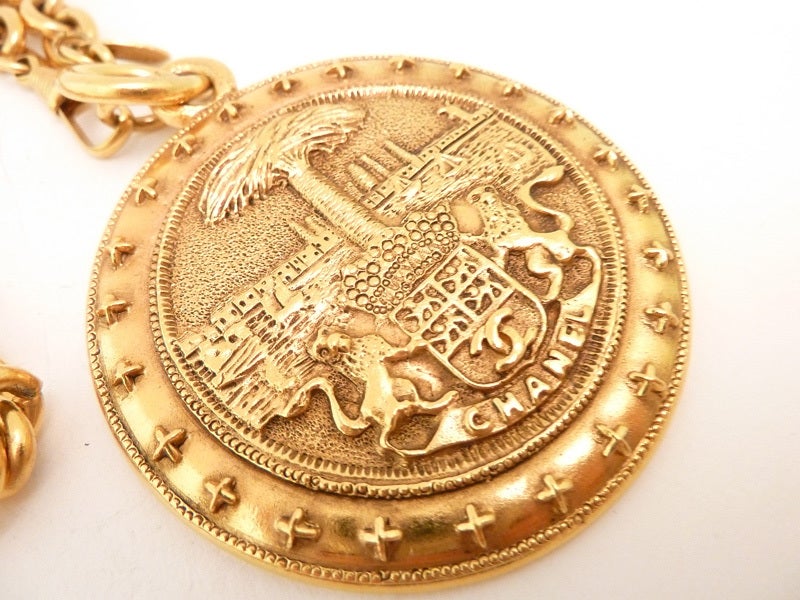 This is a substantial Chanel pendant necklace with the double-lion Chanel shield carved into the pendant in a gold-tone setting.  The pendant has a diameter of 2 3/8” and the link chain is 28” x 3/8” with a spring closure.  In excellent condition,