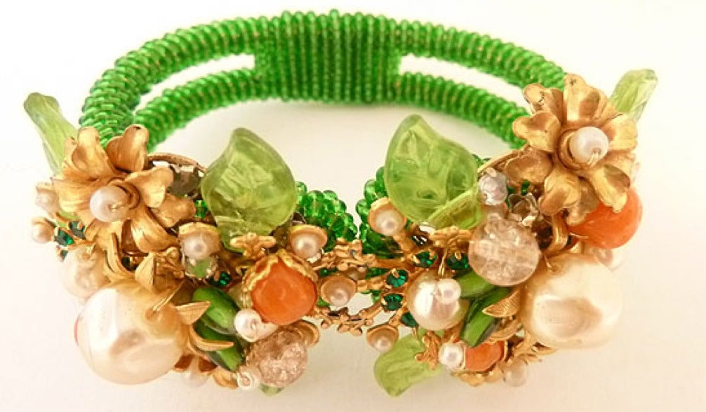 This vintage clamper bracelet features green and faux coral beads and green glass with faux pearls in a gold-tone setting. This clamper bracelet measures 6 ½? x 1 ½? and is in excellent condition.