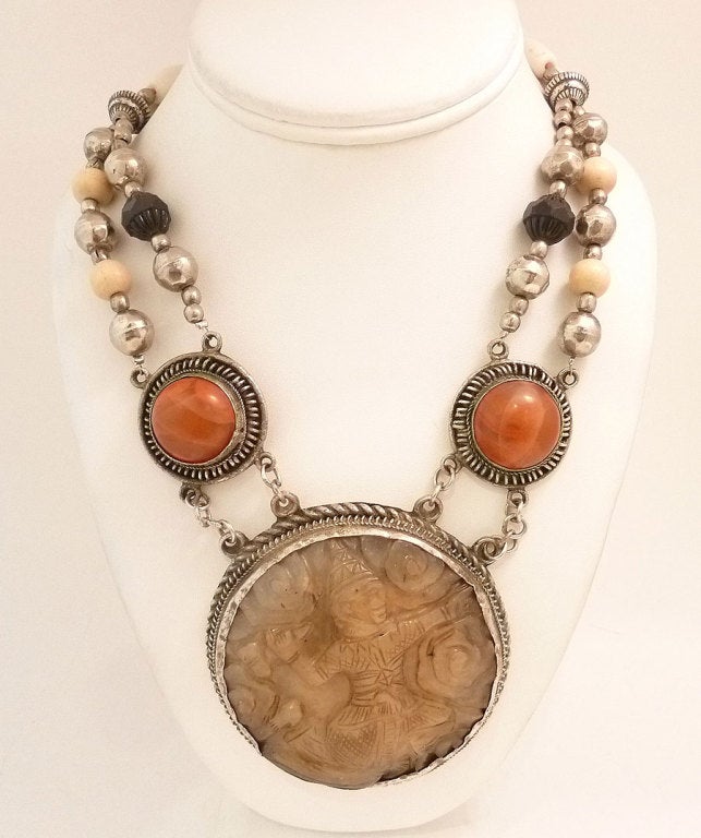 This vintage necklace features a heavily carved wide disc Jade Asian themed pendant with amber and agate bead accents in a silver-tone setting.  In excellent condition, the pendant measures 3? across and the necklace is 27? x apx ¾? with a hook
