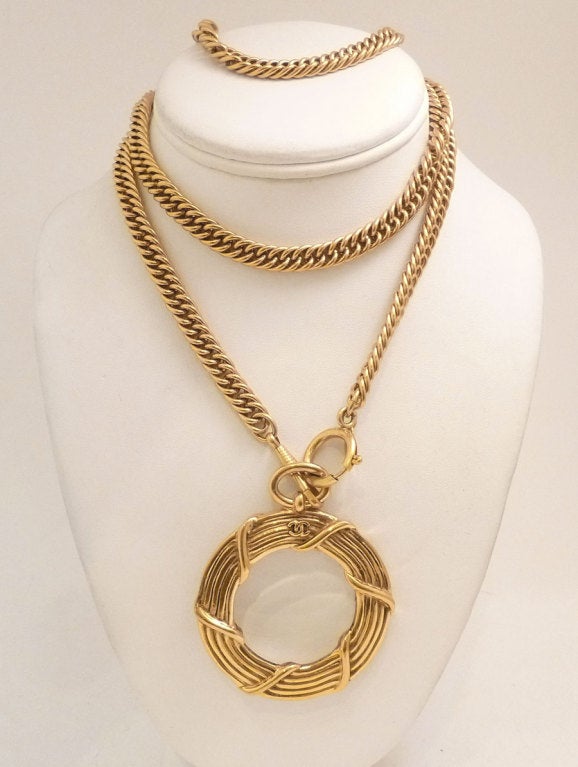 This vintage signed Chanel necklace features a magnifying glass pendant in a gold-tone setting. The bezel around the glass is twisted and forms a stunning wide frame to hold the glass in place.   In excellent condition, the pendant measures 2 5/8? x