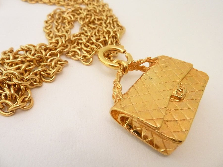 This signed Chanel necklace features the famous 3-dimensional Chanel quilted purse pendant with 3 strands of link chain in a gold-tone setting.  The pendant measures 1 5/8 inches x 1 3/8 inches.  The necklace is 29 inches with each strand being ¼?