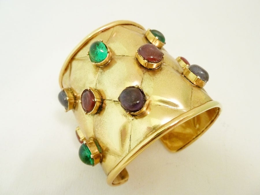 This vintage signed Chanel cuff features the famous quilted design with red, blue and green Gripoix glass cabochon stones in a gold-tone setting.  In excellent condition, this piece is adjustable and measures 7 inches x 2 3/8 inches wide and is