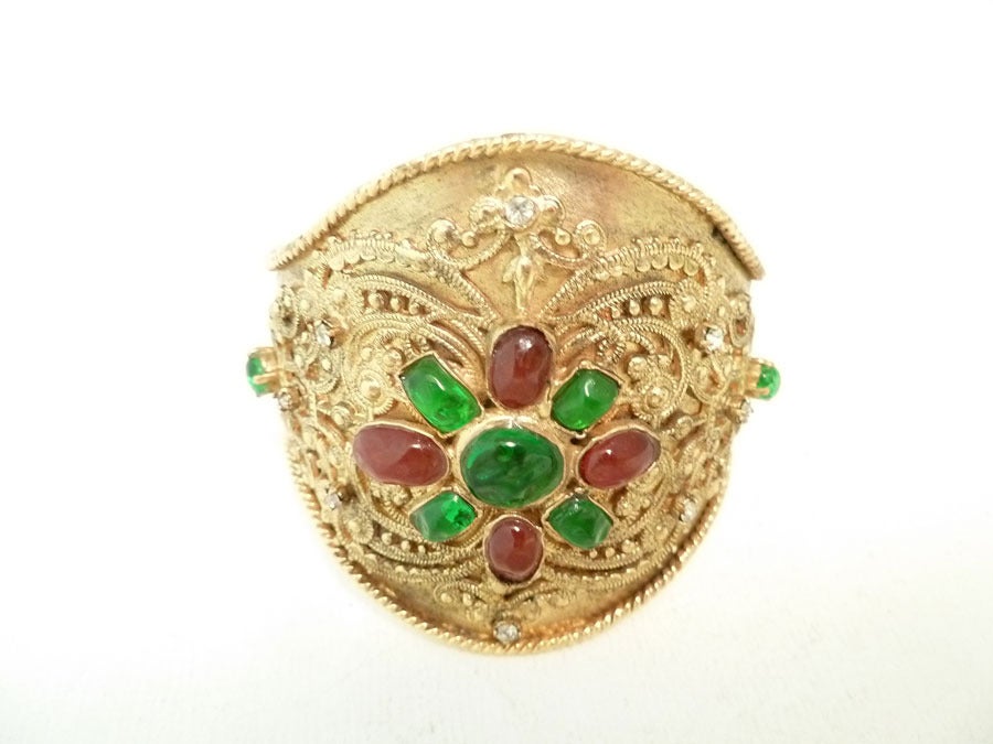 This vintage signed Chanel cuff bracelet features green and red Gripoix glass with clear rhinestone accents in a heavily carved gold-tone setting.  In excellent condition, this adjustable cuff measures 7 ¼ inches x 2 ½ inches and is signed Chanel